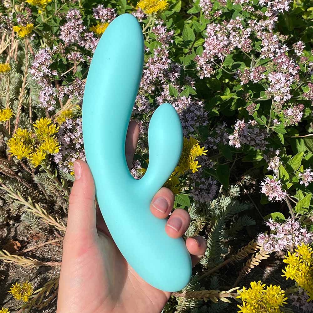 Vibrerende dildo fra Feelztoys blå, i hånd med blomster baggrund