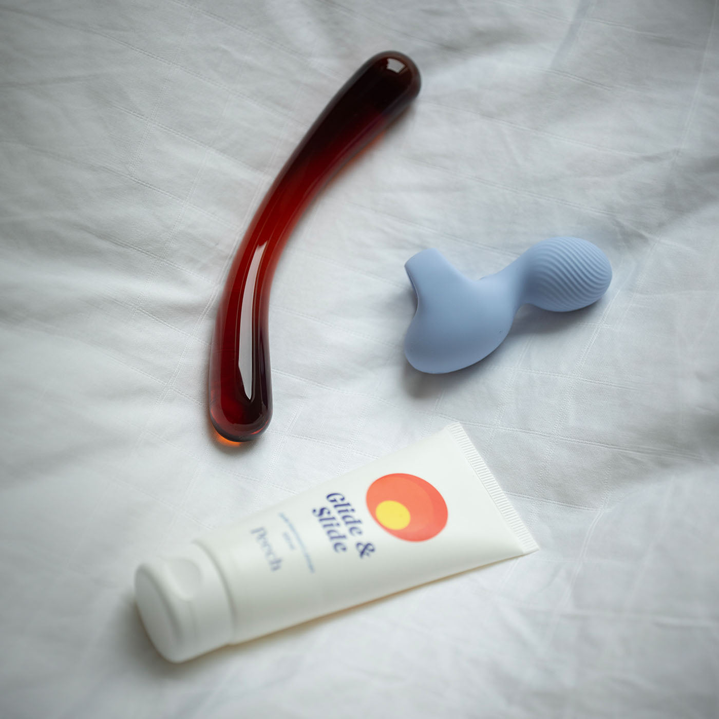 bundle med amber glasdildo, glide and slide vandbaseret glidecreme og tickly finger vibrator på seng