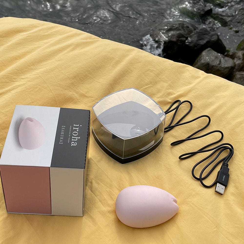 Sakura Klitoris vibrator fra Iroha by tenga, på gul baggrund og med emballage og oplader