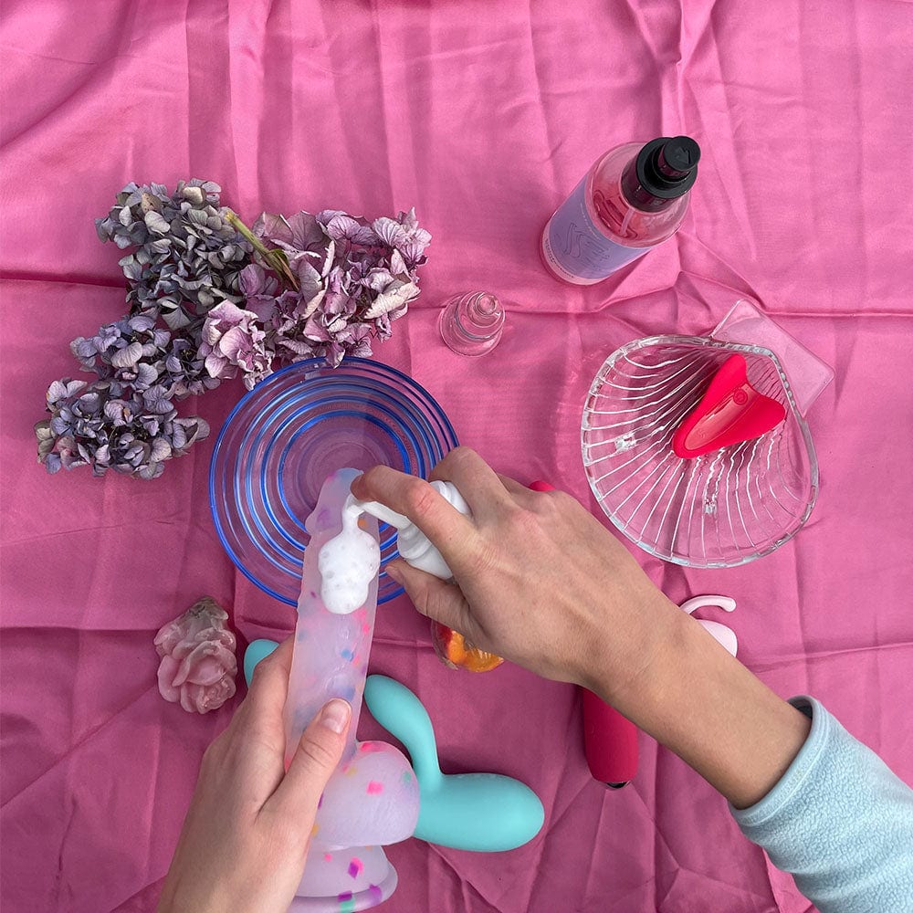 Skummende toycleaner rengøring til dit legetøj, i hånd med dildo på lyserød baggrund